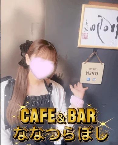 顔がぼかされた女性が写っており、背景には「CAFE & BAR ななつらぼし」という金色の文字と「WE'RE OPEN」の看板が見えます。店舗の宣伝や告知を目的とした画像です。