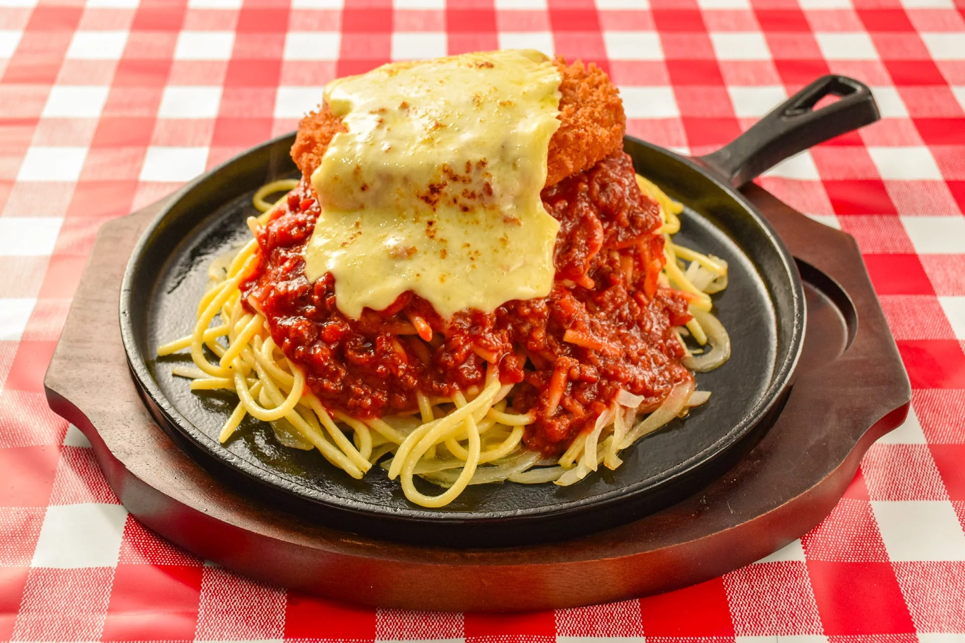 鉄板に盛られたミートソーススパゲッティの上に揚げたカツと溶けたチーズがたっぷりかかっている。