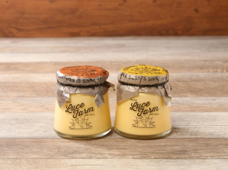 木目のテーブルに置かれたLuce Farmのプリンが2つ写っています。