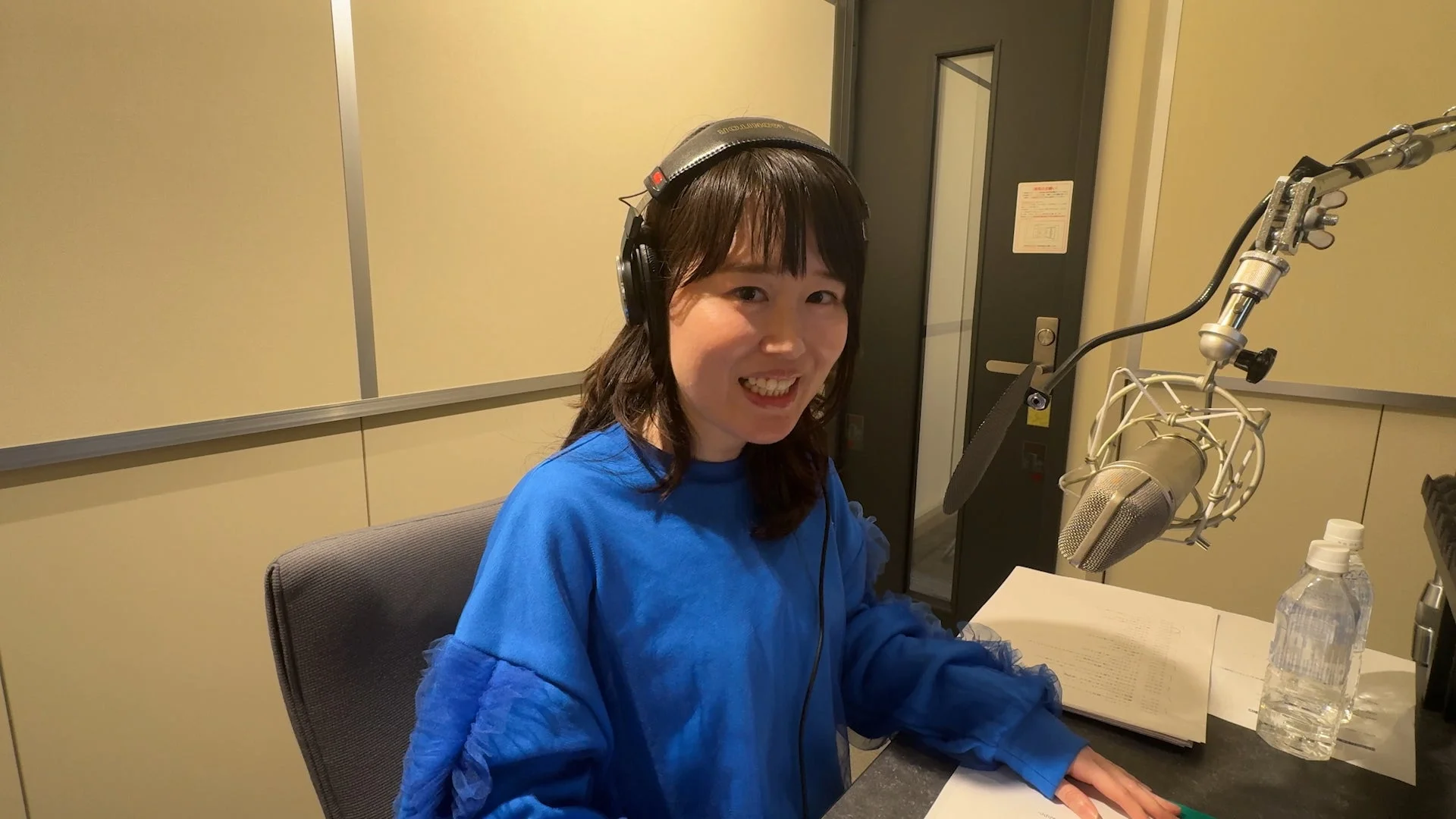 ヘッドホンを装着し、笑顔でマイクの前に座る女性の姿