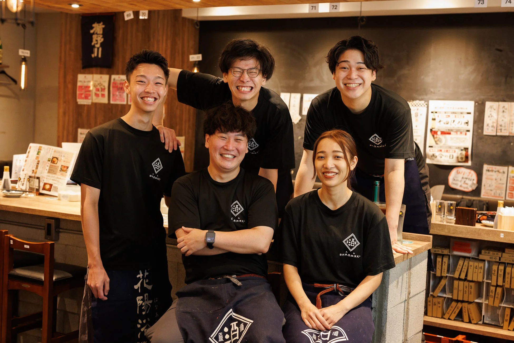 「日本酒 原価酒場」のロゴ入りユニフォームを着た男女5人の店員