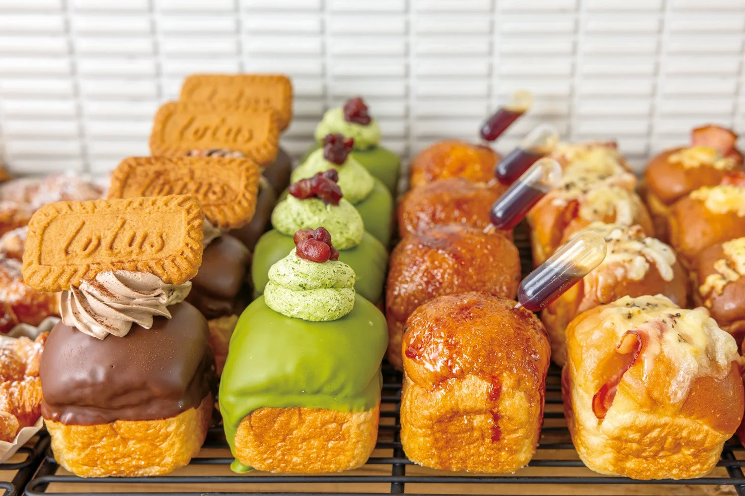様々な種類のパンやスイーツが陳列された美味しそうな写真です。チョコレートや抹茶の甘いパン、ロータスビスケットが乗ったもの、そしてチーズやハムを使った惣菜パンまで、色とりどりの豊富なラインナップが魅力です。