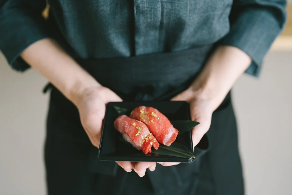 職人が両手で丁寧に差し出す、金箔が散らされた高級感あふれるマグロの握り寿司の盛り合わせ