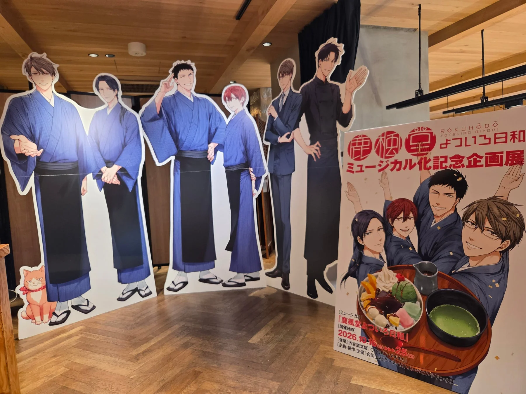 「鹿楓堂よついろ日和」のミュージカル化記念企画展の様子。和服姿のキャラクター等身大パネルや、和スイーツが描かれたポスターが展示されている。