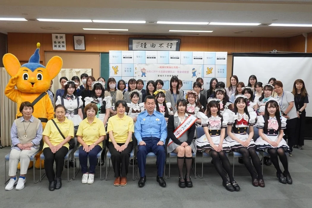 警察官、メイド服の女性たち、マスコットキャラクターの集合写真
