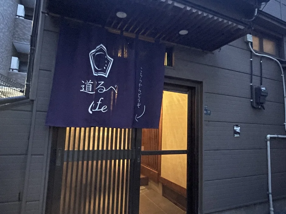 「道るべ fe」と書かれた紫色ののれんがかかる日本の建物の入り口