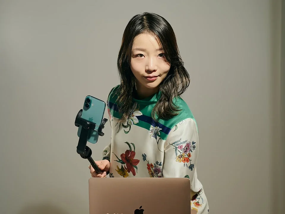 花柄のシャツを着たアジア人女性がスマートフォンを持っている様子