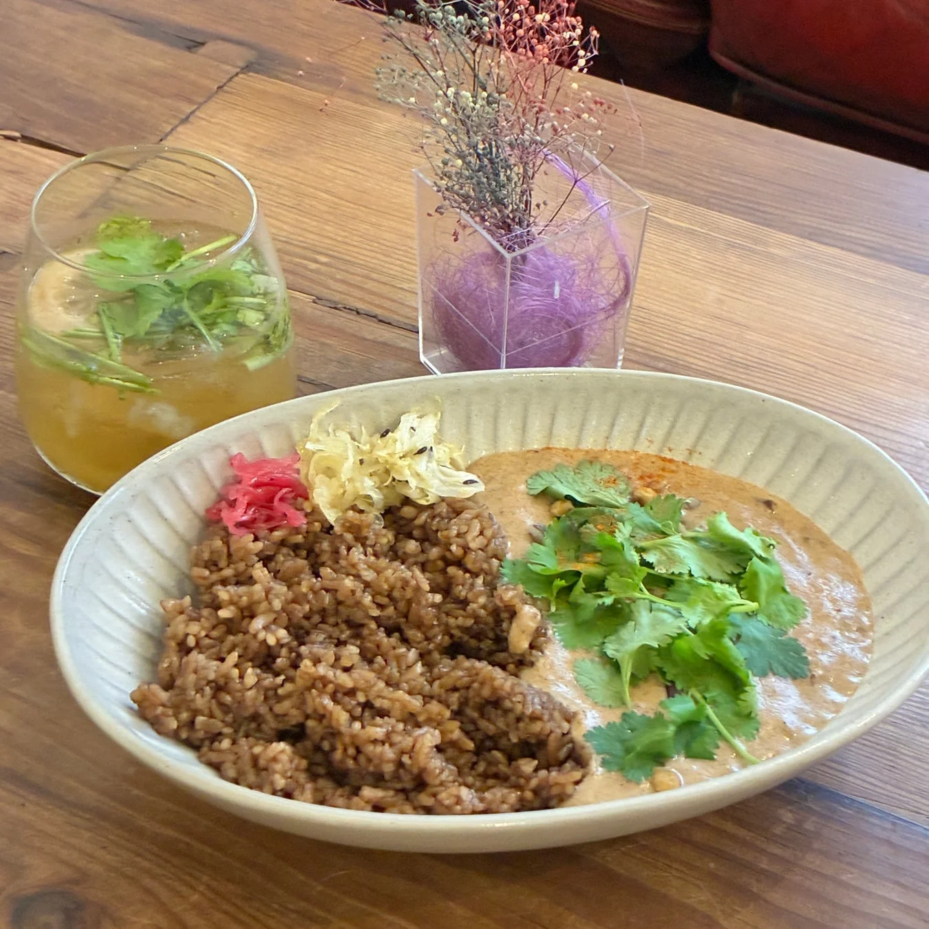 木製のテーブルに置かれた、パクチーが添えられたカレーライスと、生姜のピクルス