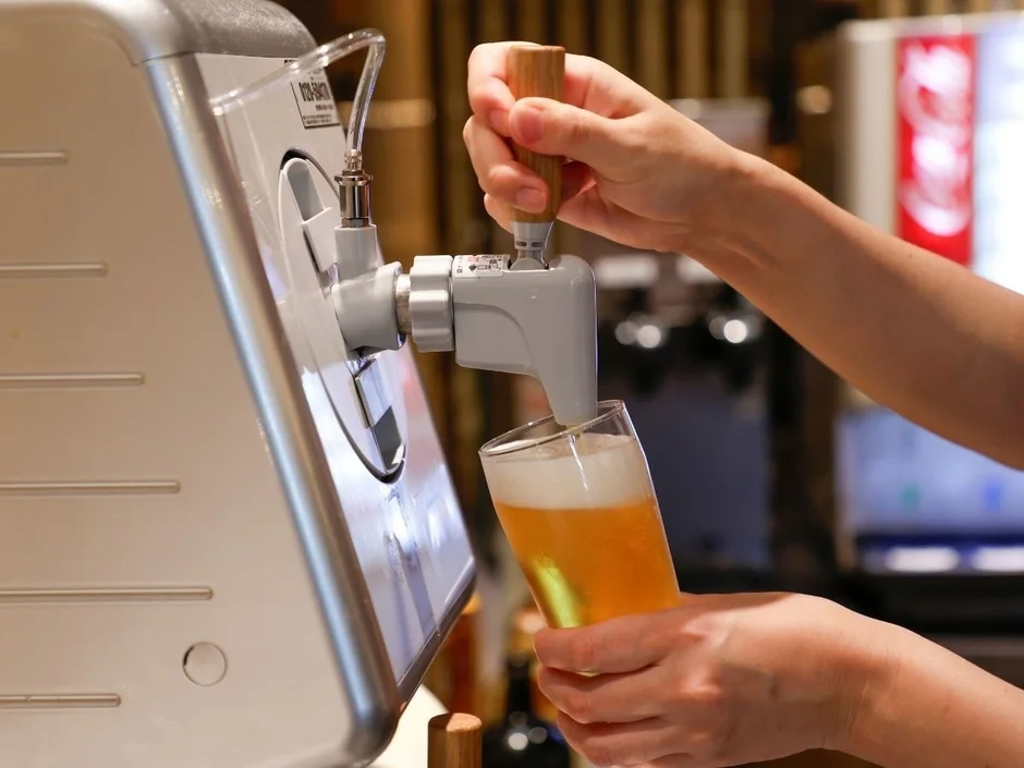 人がドリンクディスペンサーを操作し、グラスに泡立つビールを注いでいる瞬間