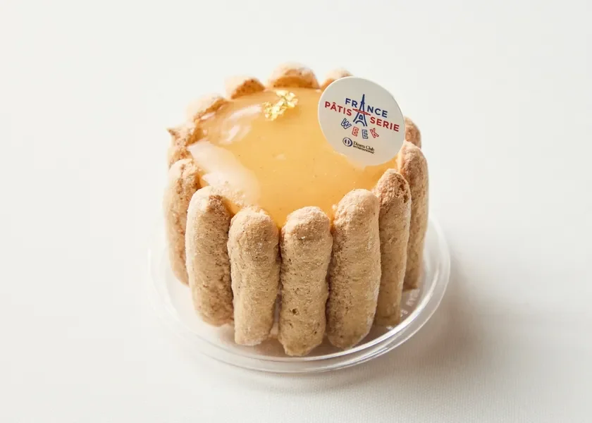 白い背景に置かれた、ビスキュイ生地で囲まれたフランス風の美しいケーキです。上部には艶やかなムースと金箔が飾られ、「FRANCE PÂTISSERIE WEEK」と書かれたロゴピックが添えられています。