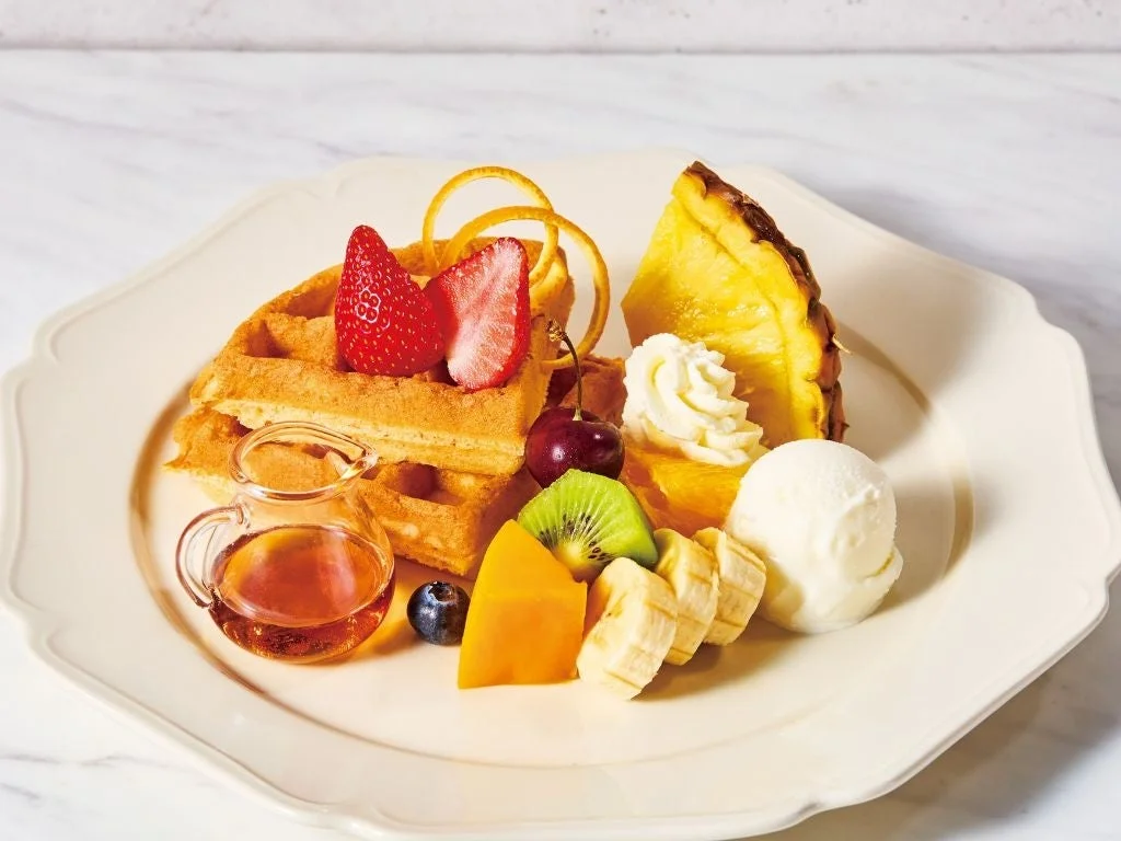 白い皿に盛り付けられた、焼きたてのワッフルと色とりどりのフルーツ、ホイップクリーム、バニラアイスクリーム