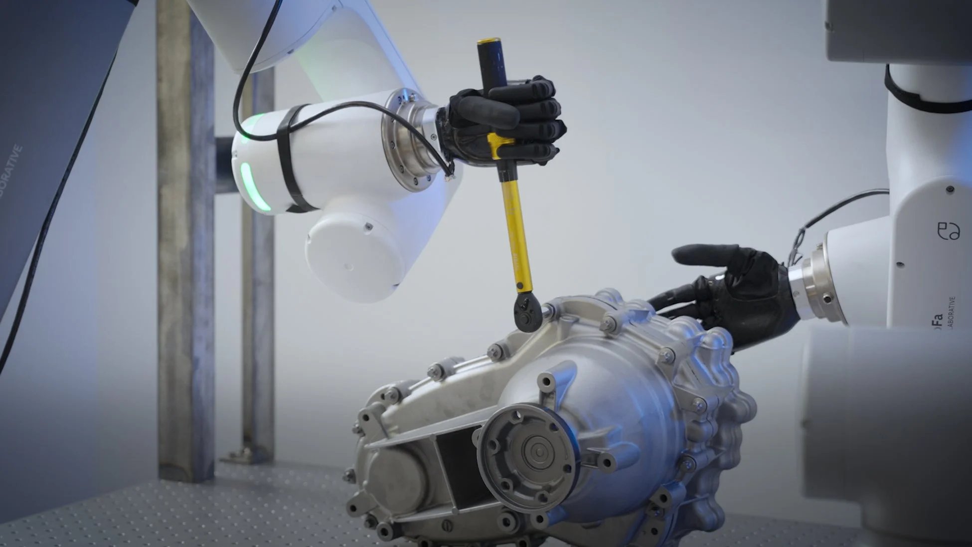 2台の産業用ロボットアームが、それぞれ工具を持ち、自動車のギアボックスのような機械部品を扱っている様子を捉えた画像です。自動化された製造工程を示唆しています。