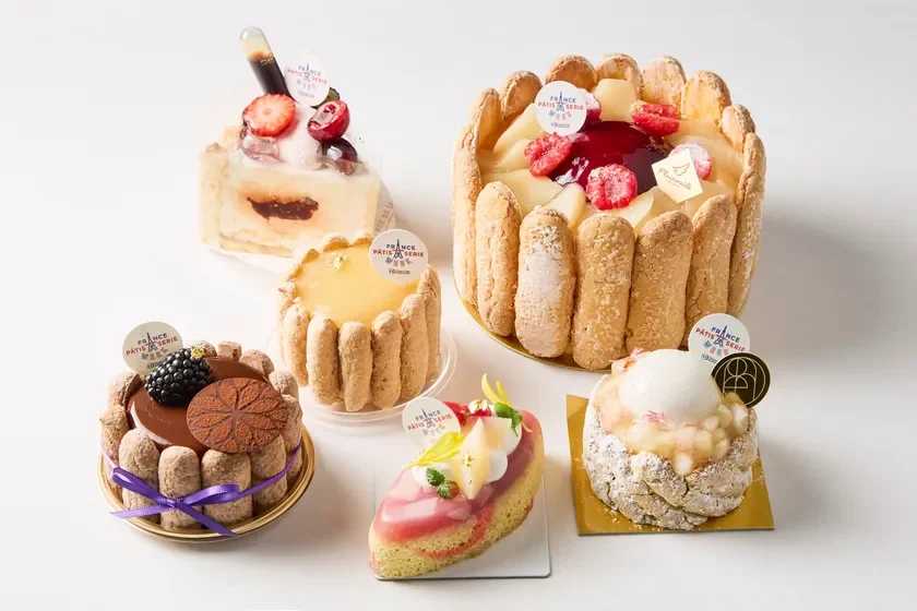 白背景に美しく盛り付けられた、色とりどりのフランス菓子が複数並べられています。フルーツやチョコレートで飾られた様々な種類のケーキやタルトが見られ、特別なイベントや贈り物にぴったりの華やかなデザートの集合です。