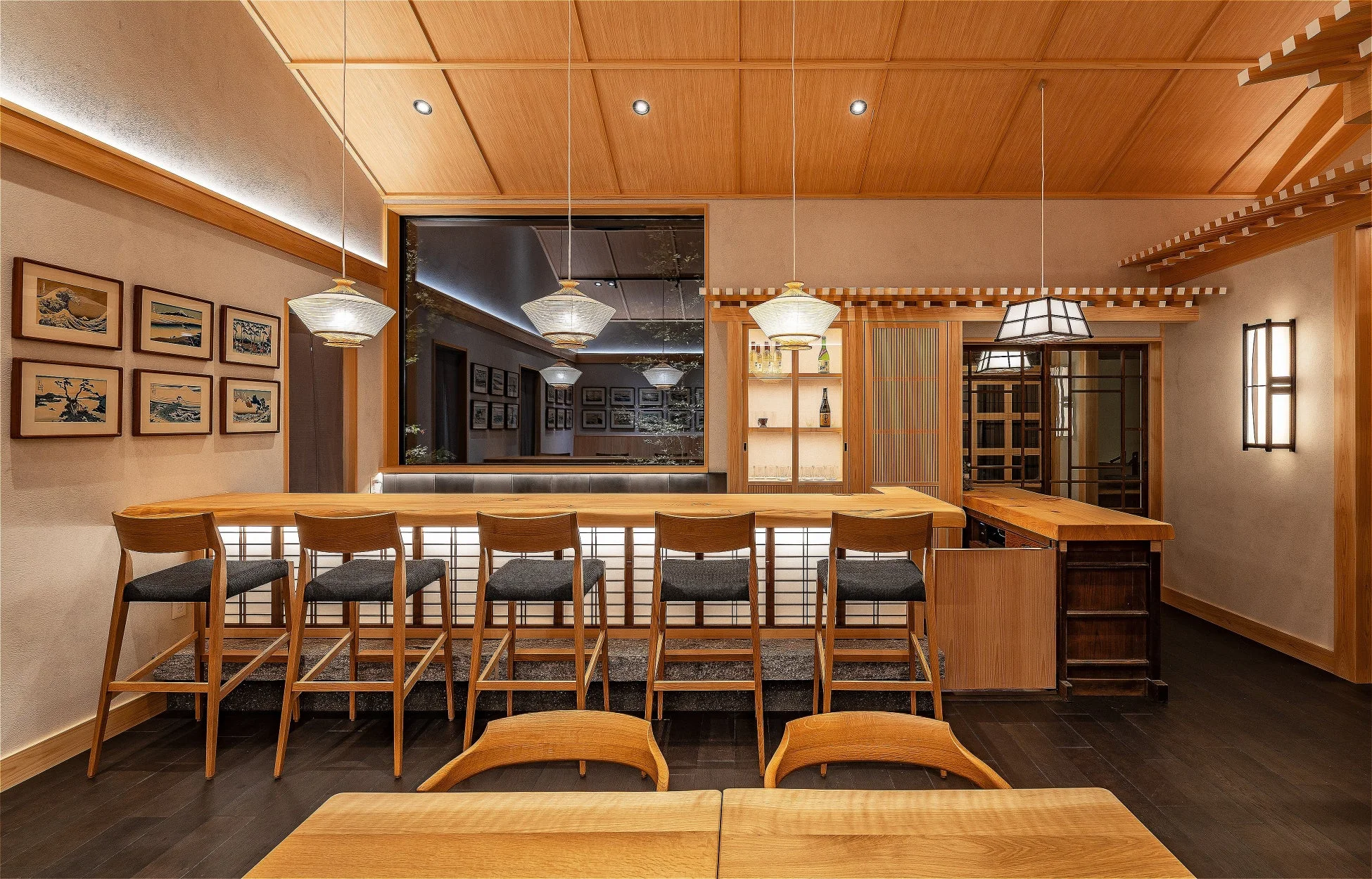 木製のカウンター席が並ぶ、温かみのある和風バーまたは日本料理店の内装です。壁には浮世絵が飾られ、落ち着いた雰囲気を醸し出しています。