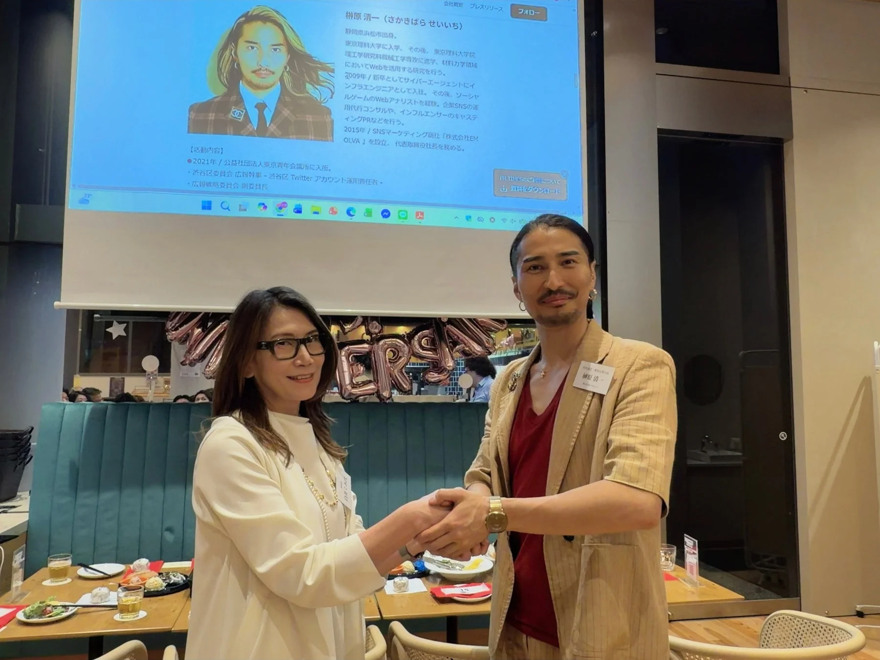 榊原氏と女性が握手するビジネスイベントの様子
