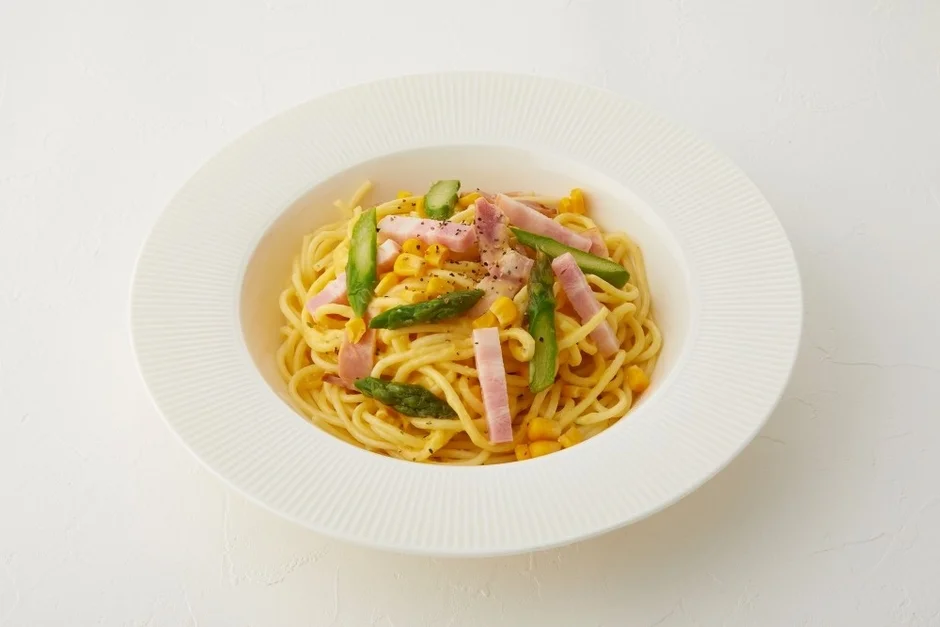 アスパラガス、ハム、コーンがトッピングされたクリームベースのパスタ