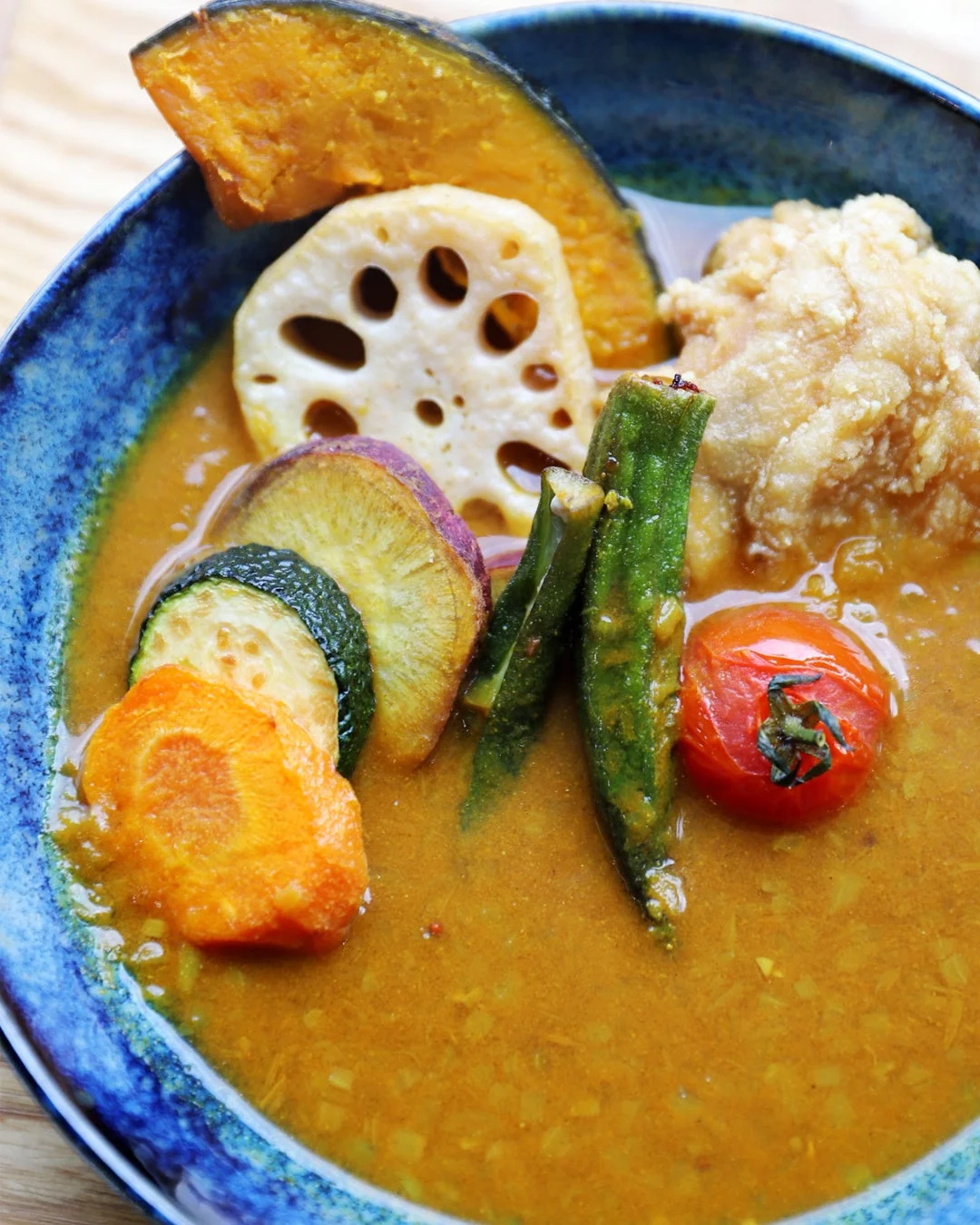色鮮やかな野菜と揚げ物がたっぷりと入った、食欲をそそるスープカレーです。かぼちゃ、レンコン、オクラ、トマト、さつまいも、ズッキーニ、ニンジンなど様々な具材が使われています。