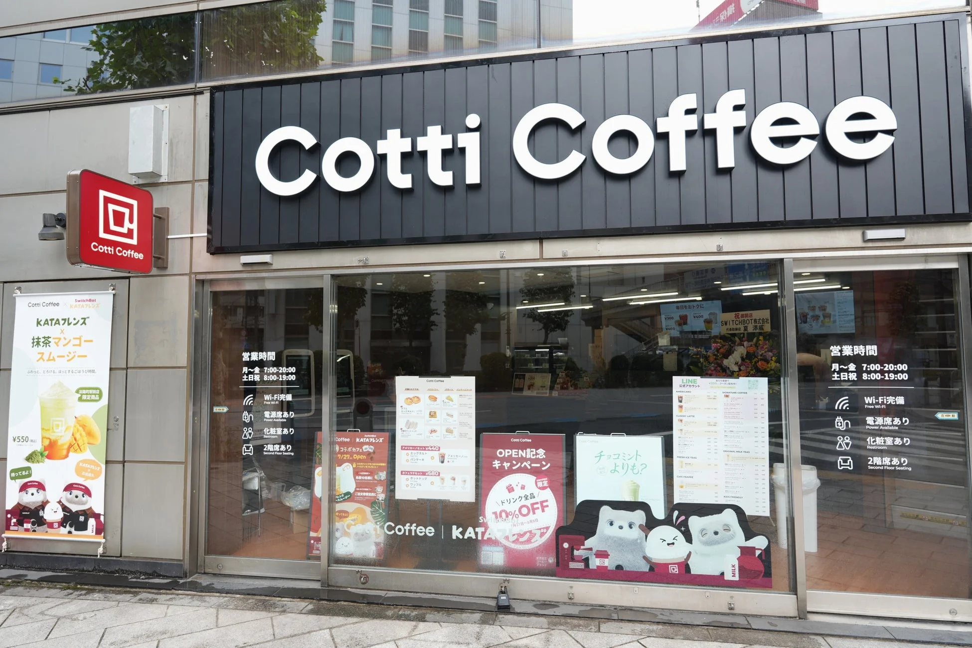 「Cotti Coffee」の店舗外観。抹茶マンゴースムージーやKATAフレンズとのコラボ、開店記念のドリンク10%オフキャンペーンを告知。Wi-Fi、電源席、化粧室、2階席が完備されており、営業時間は月～金7:00-20:00、土日祝8:00-19:00。