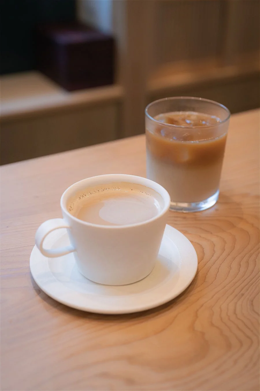 木製のテーブルに、温かいカフェラテと氷の入ったアイスコーヒーが並べられています。カフェでの穏やかなひとときを感じさせる、落ち着いた雰囲気の画像です。