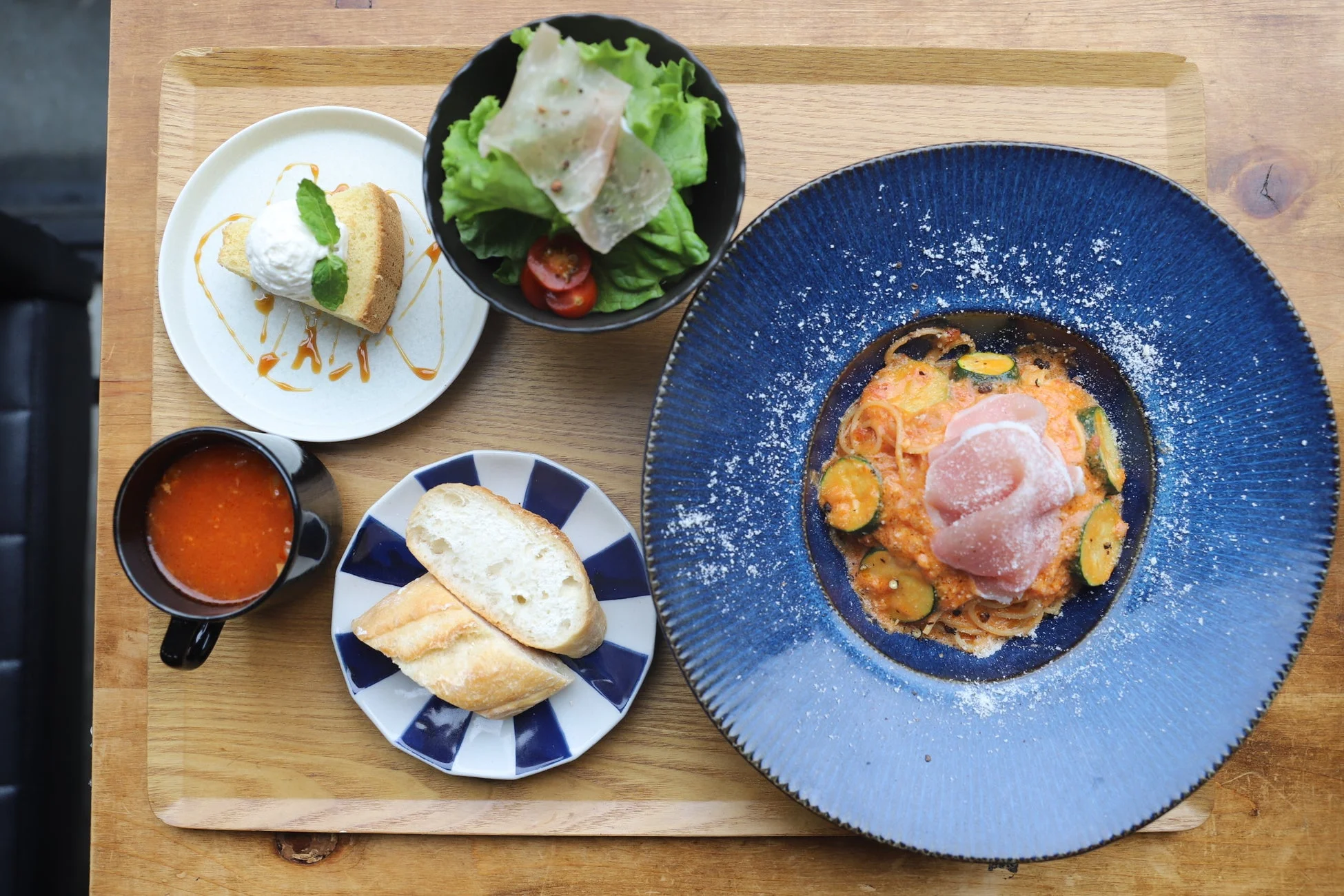 木製のトレイに盛られたランチセット。メインのパスタ、サラダ、スープ、パン、そしてデザートのシフォンケーキが美しく配置されており、カフェでの食事風景を捉えた一枚です。