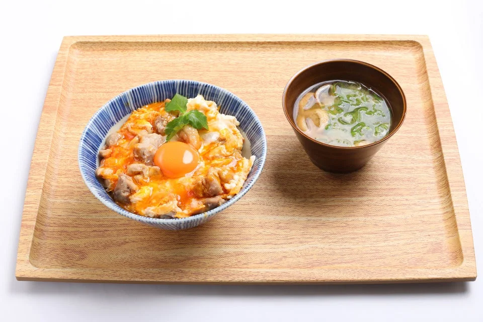 木のトレーに盛り付けられた親子丼と汁物の和食セット