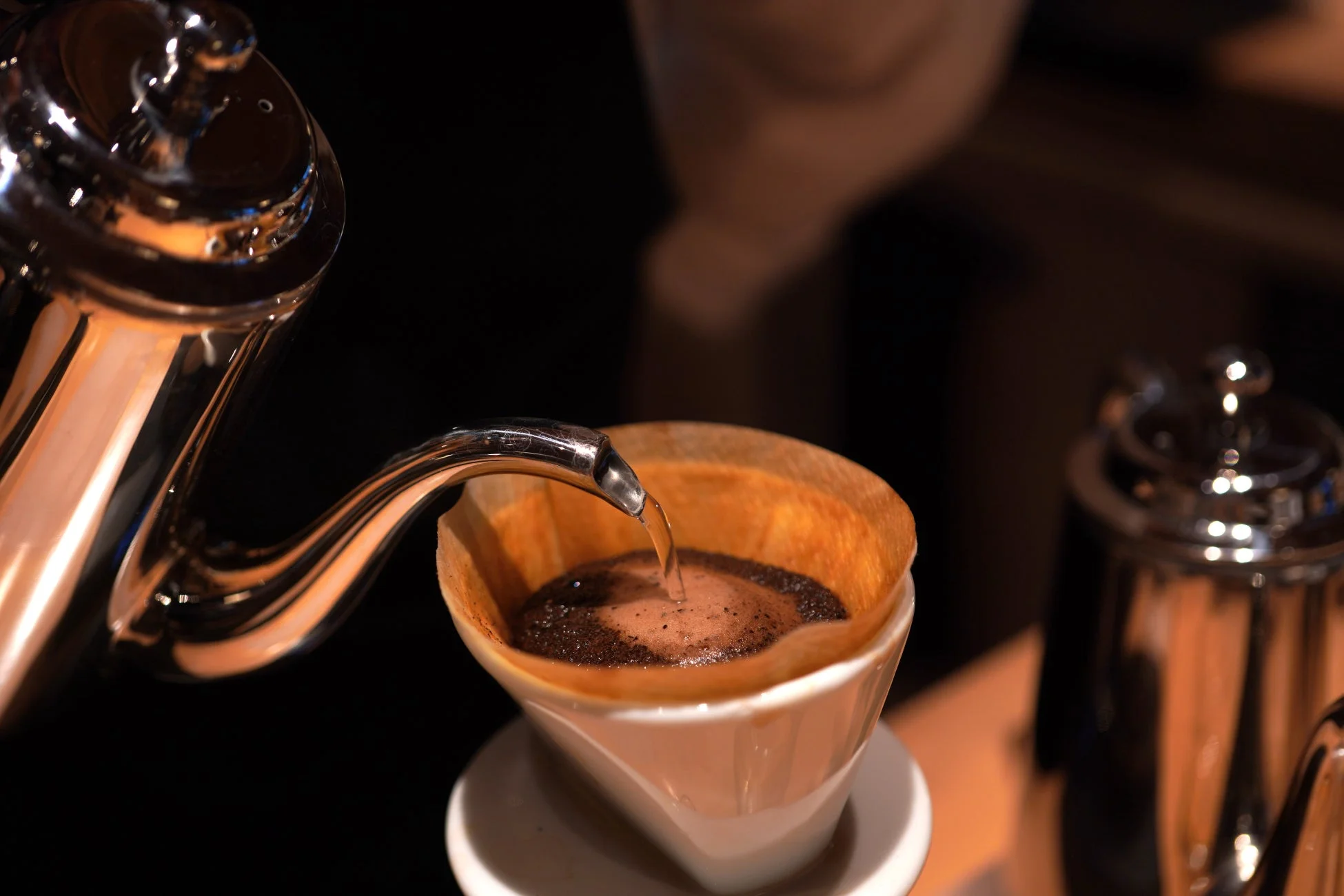 銀色のケトルからお湯が注がれ、コーヒーフィルターに入った粉が膨らみ、ドリップコーヒーが抽出されている様子を捉えた写真です。丁寧にコーヒーを淹れる瞬間が表現されています。