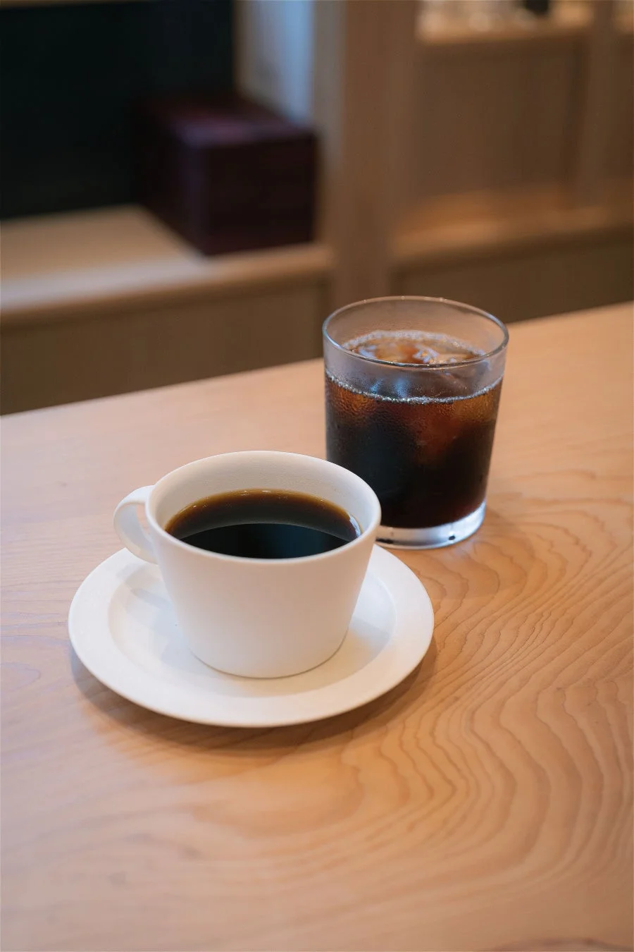 木製のテーブルに置かれたホットコーヒーとアイスコーヒー。落ち着いた雰囲気のカフェで、くつろぎのひとときを過ごしている様子が伺えます。