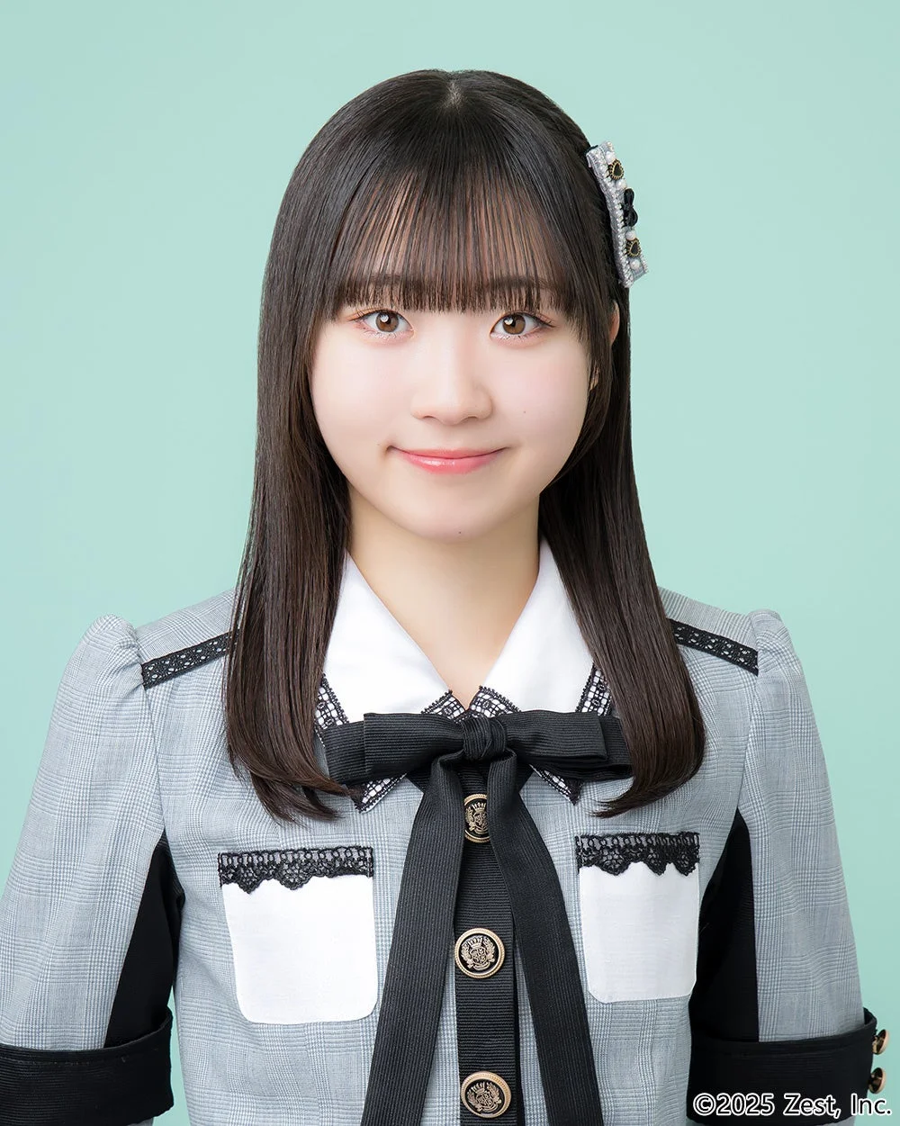 制服のようなグレーのジャケットと大きな黒いリボンを着用した若い日本人女性が、優しく微笑んでいるポートレート写真