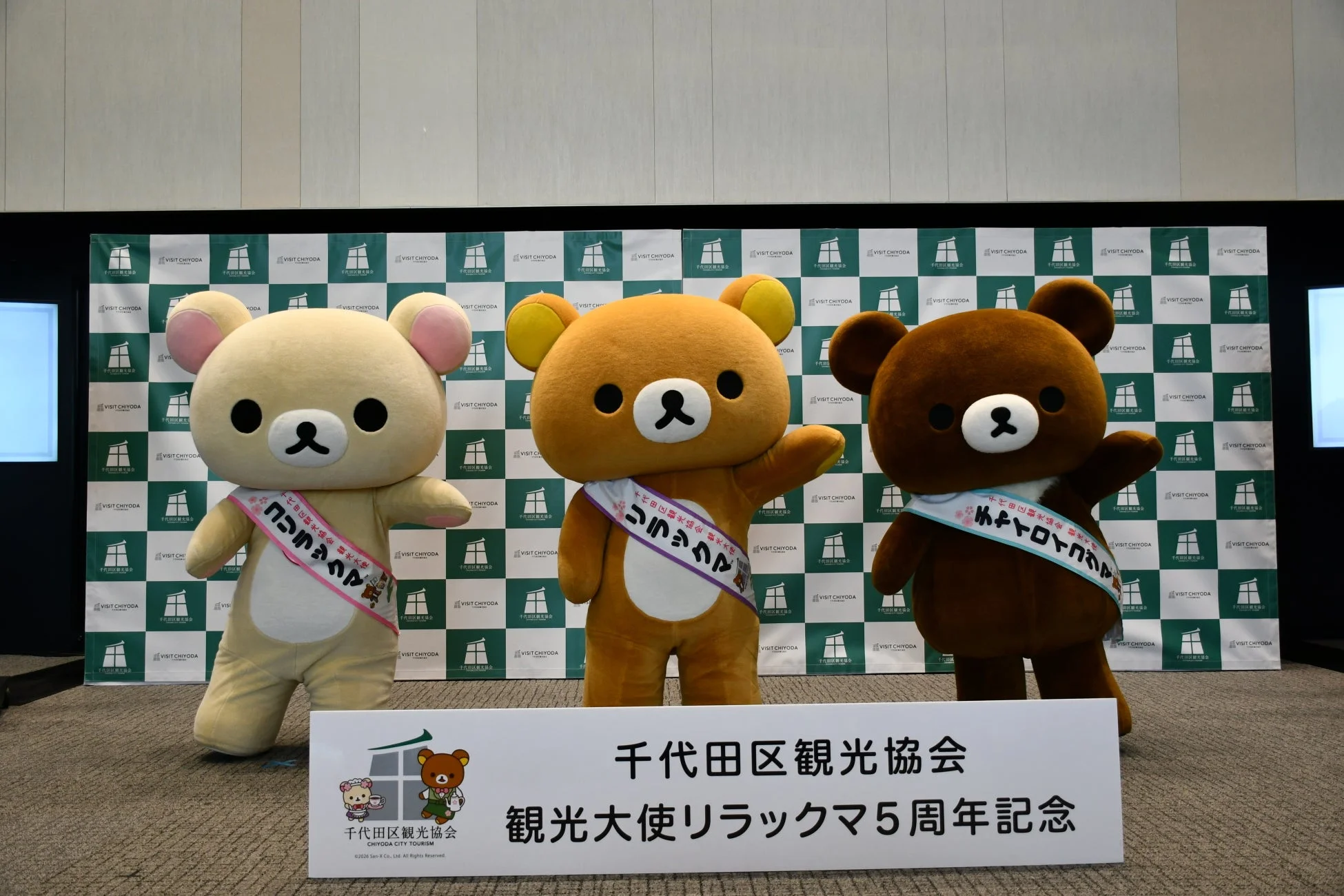 千代田区観光大使リラックマの5周年記念イベントで、コリラックマ、リラックマ、チャイロイコグマの3体がステージに並んでいます。背景には千代田区観光協会のロゴが見えます。