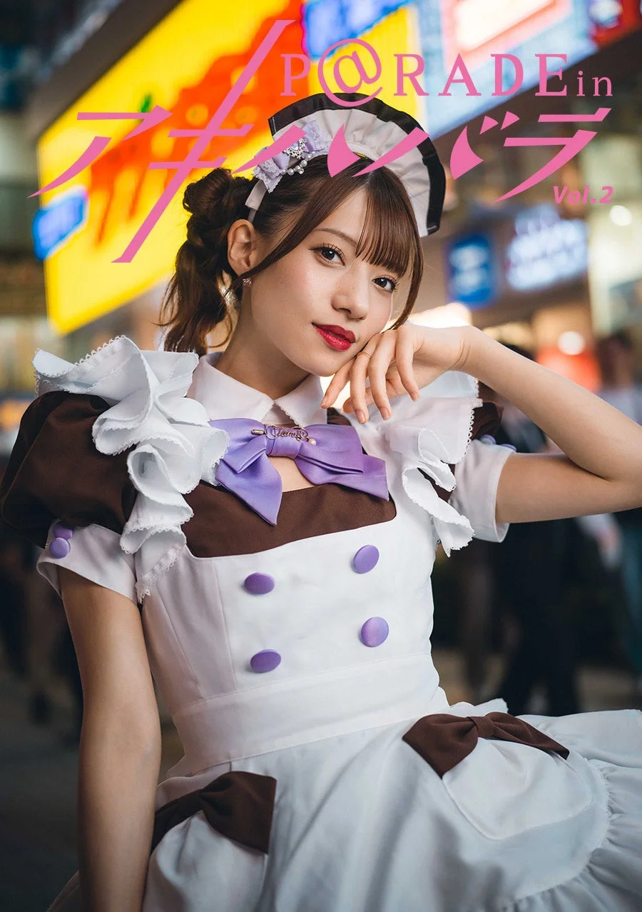 メイド服を着た日本人女性が、アキバの街を背景に魅力的なポーズをとっている。