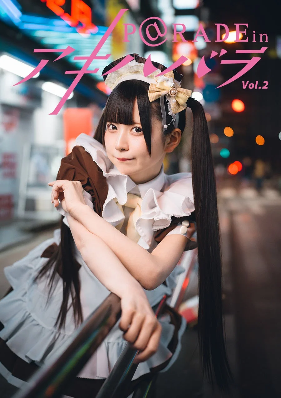 メイド服を着たツインテールの日本人女性が、夜の街並みを背景にポーズをとっている画像です。