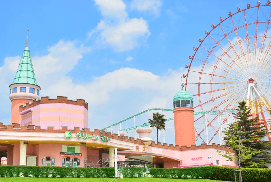青空の下、ピンクとオレンジ色の建物が特徴的な遊園地の風景