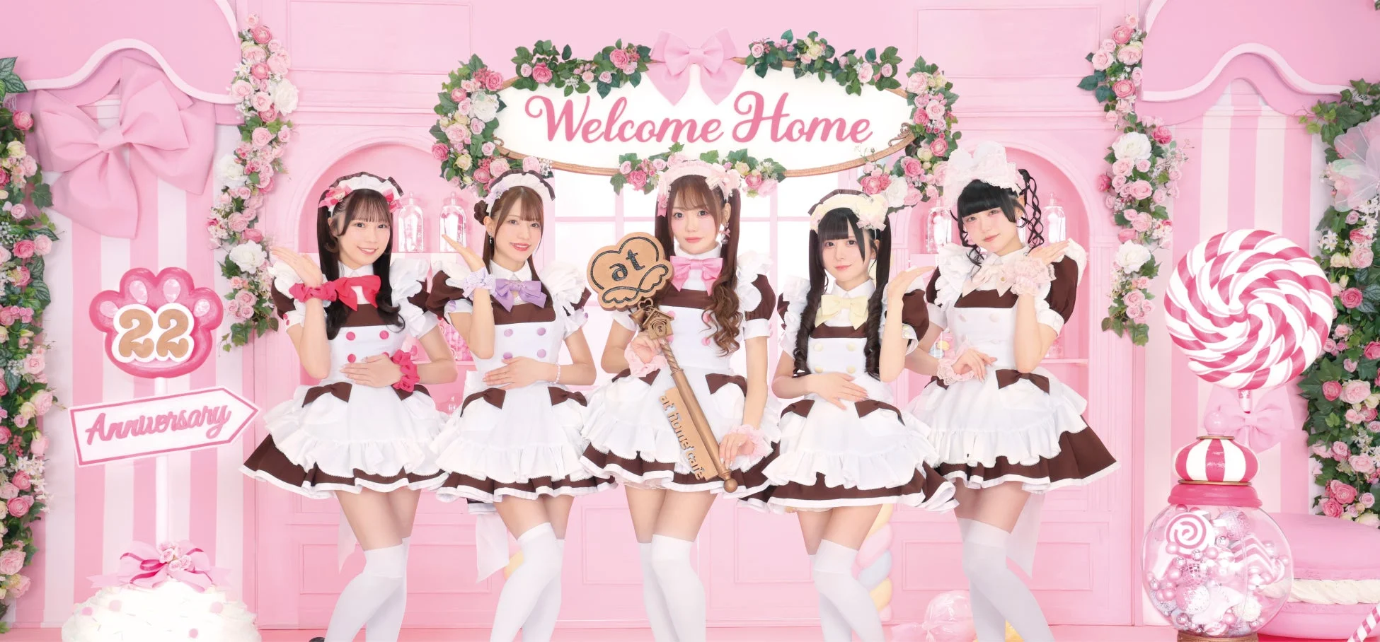 ピンクを基調とした可愛らしい空間で、ブラウンとホワイトのメイド服を着た5人の女性がポーズをとっています。