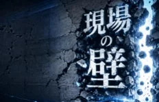 暗い壁が中央で大きくひび割れ、そこから青白い光が漏れ出している画像です。壁には「現場の壁」という文字が書かれており、何かの障壁を打ち破るような力強い印象を与えます。