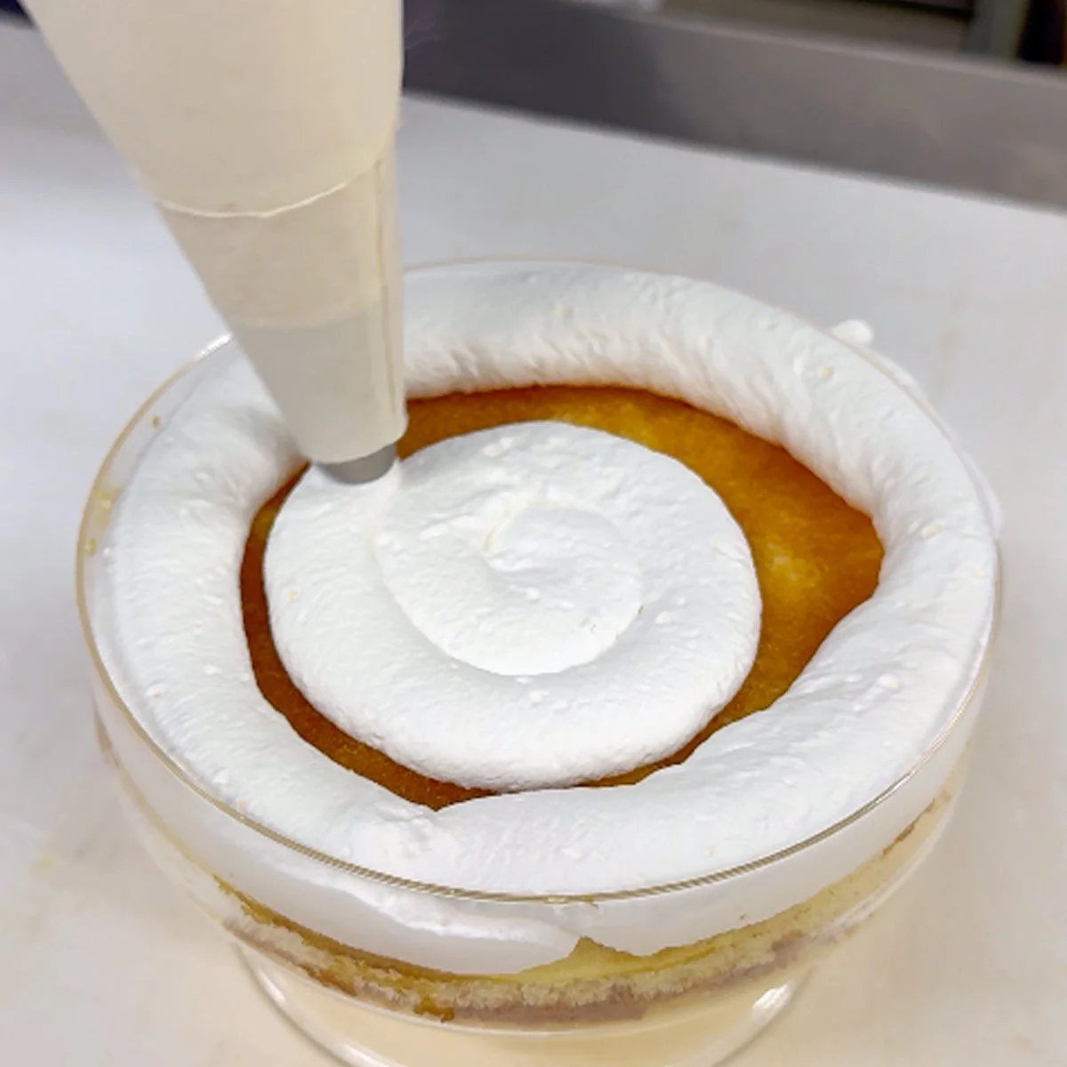 透明なカップに入ったケーキの上に、絞り袋を使って白いホイップクリームが渦巻き状にデコレーションされている