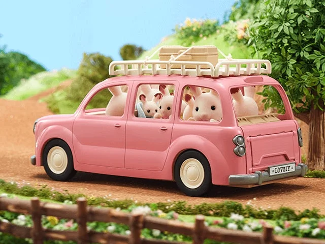 ピンクのミニチュアワゴン車が土の道を走っており、車内には複数の可愛らしいウサギのフィギュアが乗っています。屋根には荷物が積まれ、家族でのドライブや旅行を思わせる、のどかな風景が描かれています。