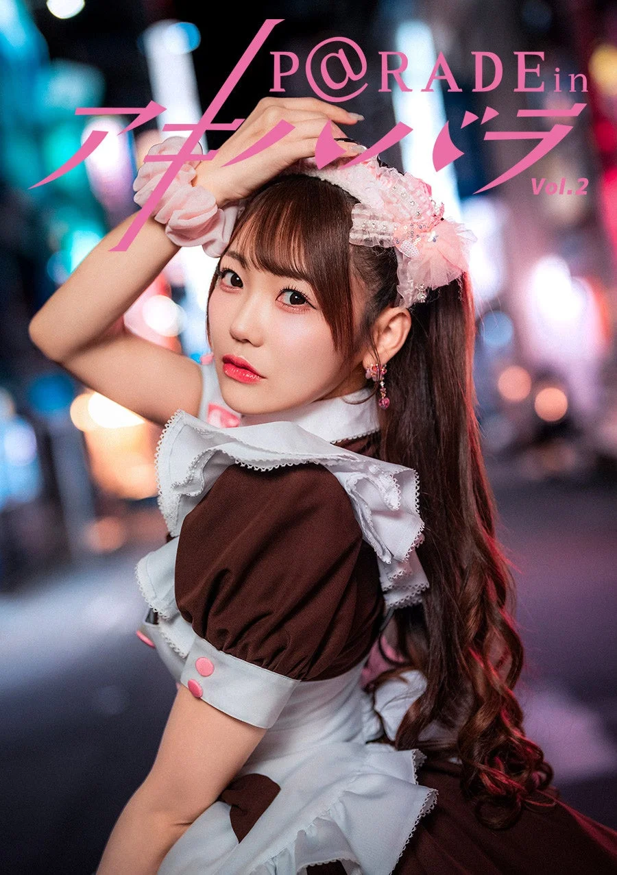 メイド服を着た若い女性が、夜の街を背景にカメラ目線でポーズをとっています。